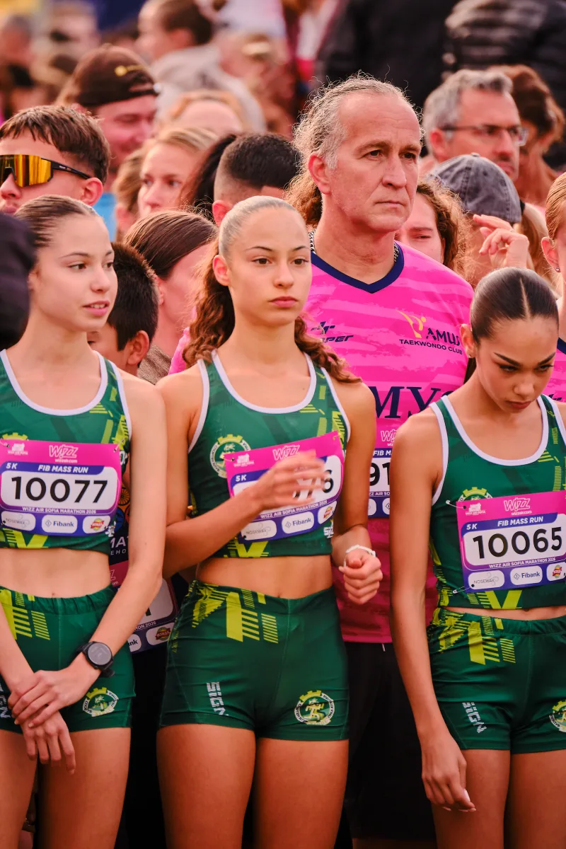 Runners in green vests and pink shirts waiting in a packed crowd.