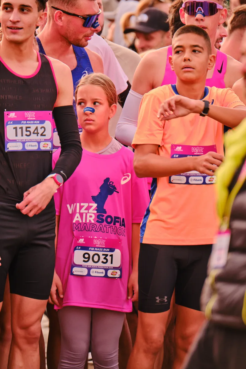 Young participants in black and pink tops standing among runners.