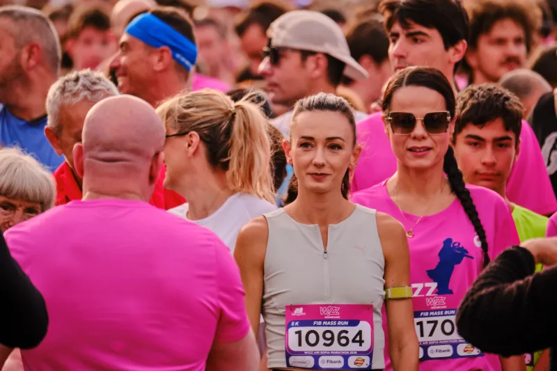 A runner in a pale vest waits among people wearing bright pink.