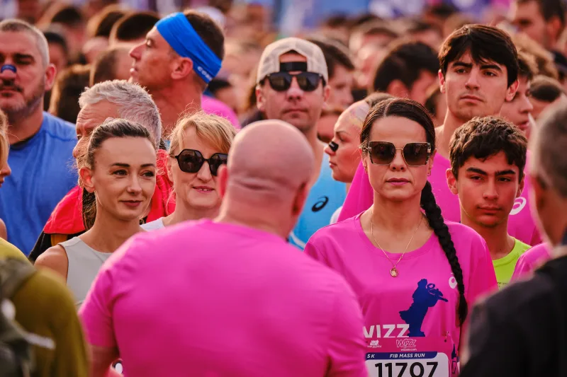 A woman in sunglasses and a pink event shirt in the crowd.