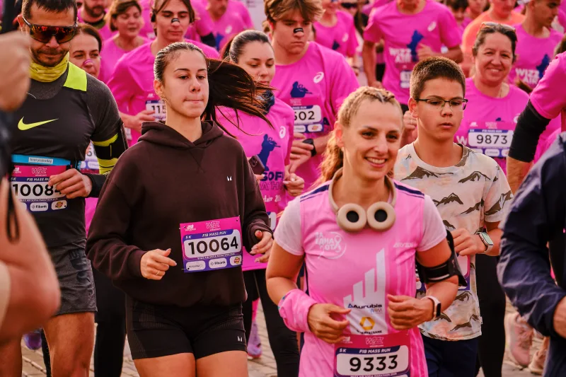 A smiling runner with headphones around her neck among people in pink.