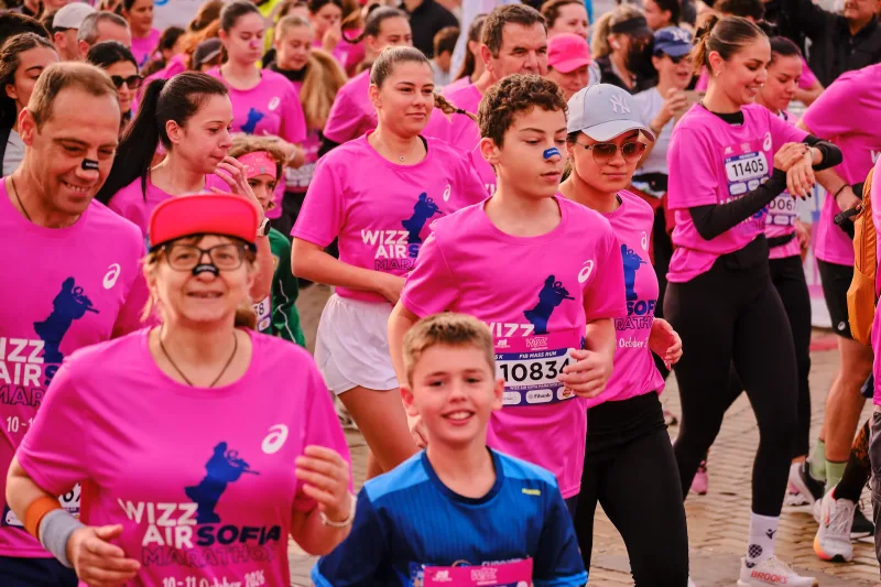 A child and an older runner moving through the crowd in pink event shirts.