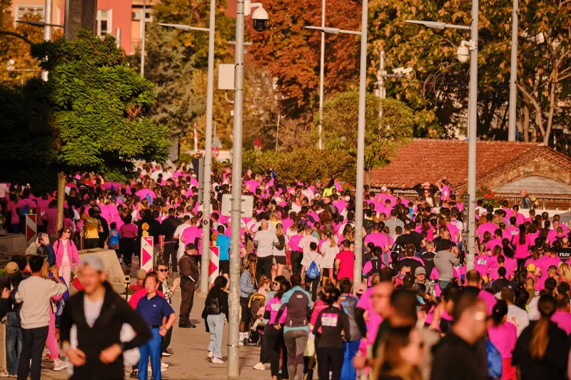 A sea of pink event shirts beneath autumn trees and flagpoles.