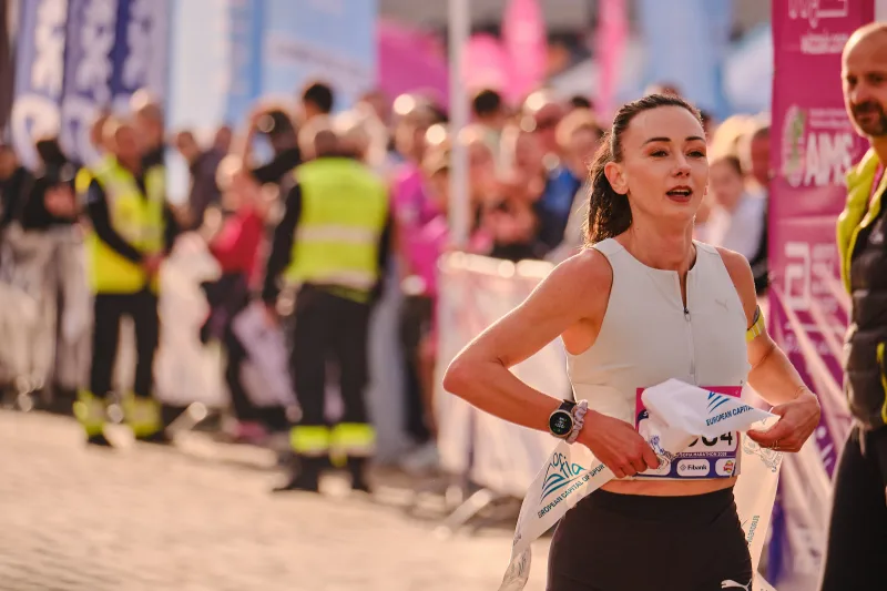 A runner in a pale sleeveless top moving past the event barriers.