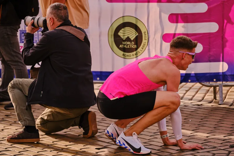 A runner in a pink vest crouching on the cobbled square.