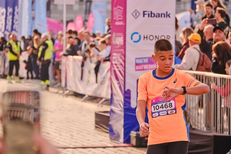 A young runner in an orange vest looking at his wrist.