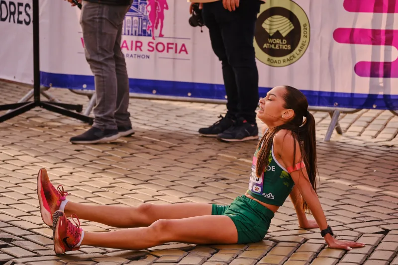 A runner in green sitting on the cobblestones with legs stretched out.