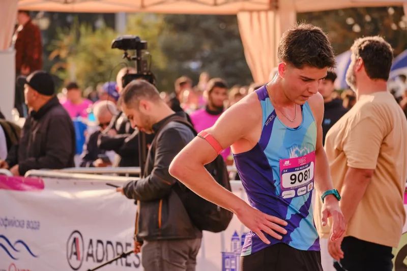 A runner in a blue vest standing beside spectators and barriers.