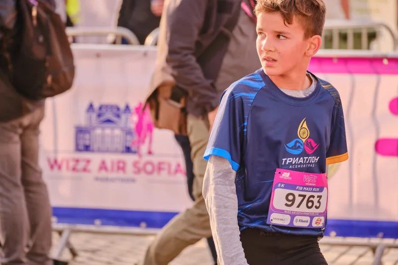 A young participant in a navy sports shirt beside a pink banner.