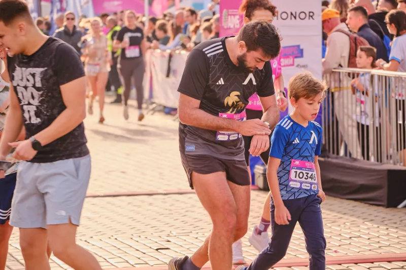 A runner in a dark top moving beside a young participant in blue.