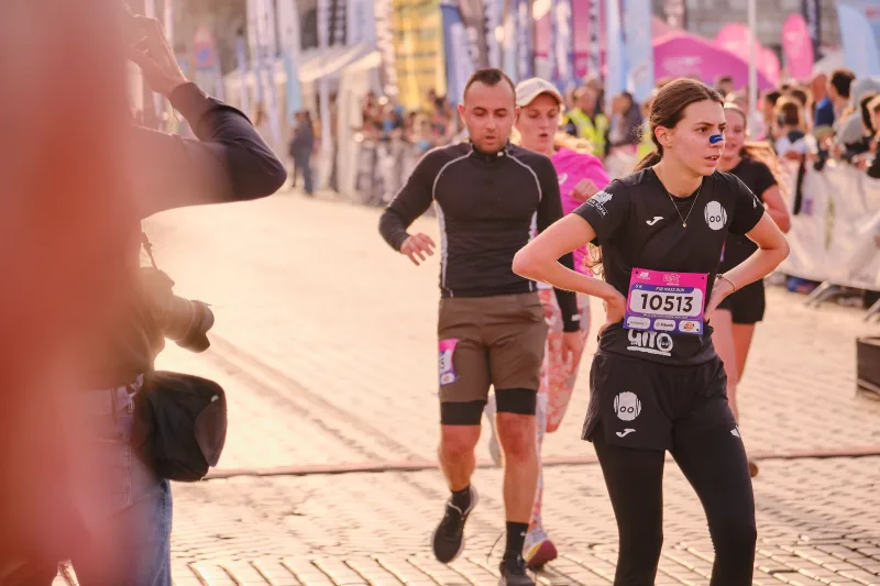 Two runners in black approaching past the event barriers.