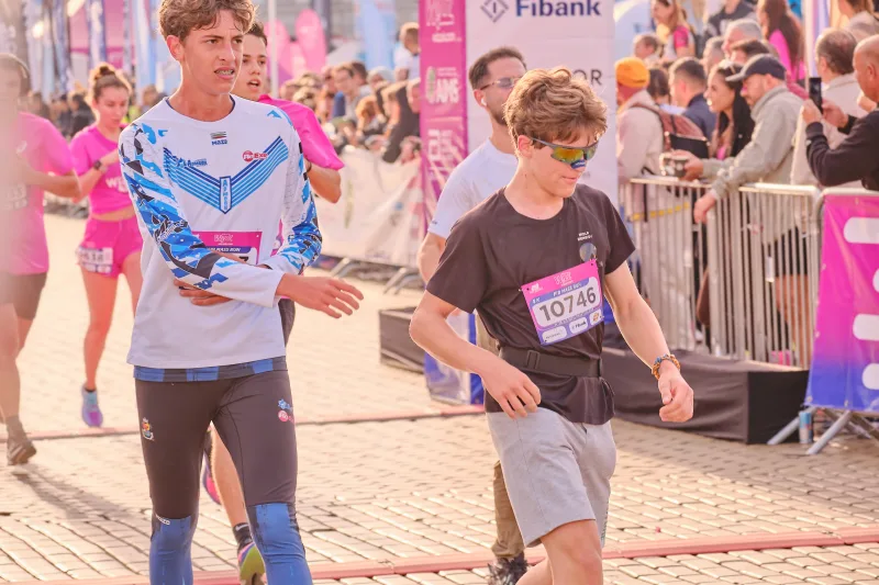 A participant in a patterned blue top beside a young runner in black.