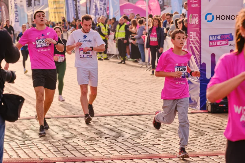 Runners passing the pink banners with spectators behind the barriers.