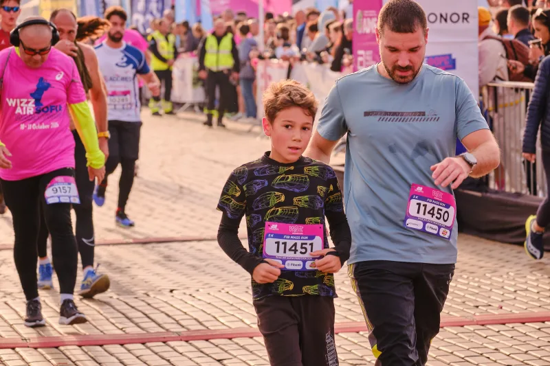 A man in grey running beside a young participant in a dark shirt.