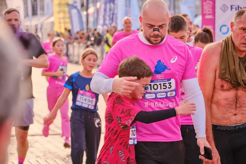 A runner in pink looking at his watch as he passes the camera.