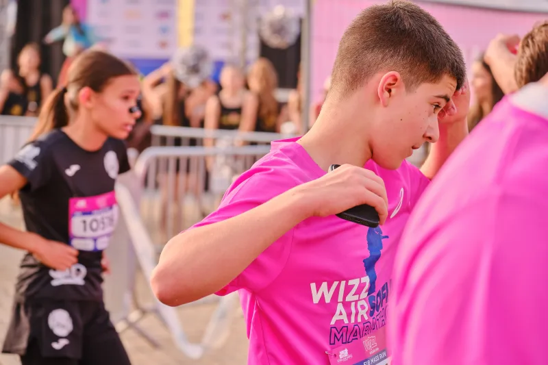 A young participant adjusting the collar of his pink event shirt.