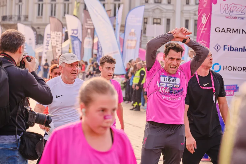 A runner in pink raising both arms as he approaches the event area.