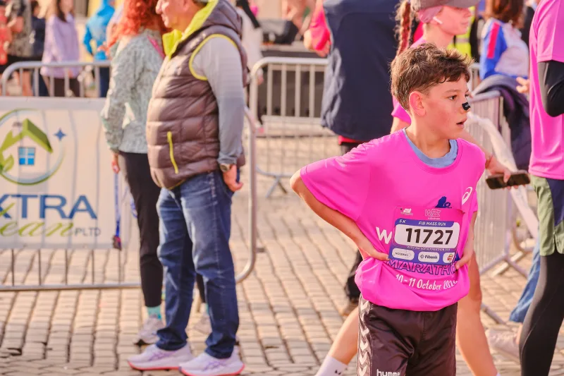 A young runner in pink standing with hands on hips near the barriers.