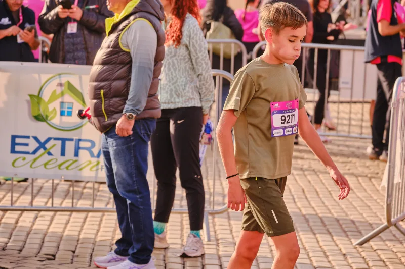 A young participant in an olive shirt beside the race barriers.