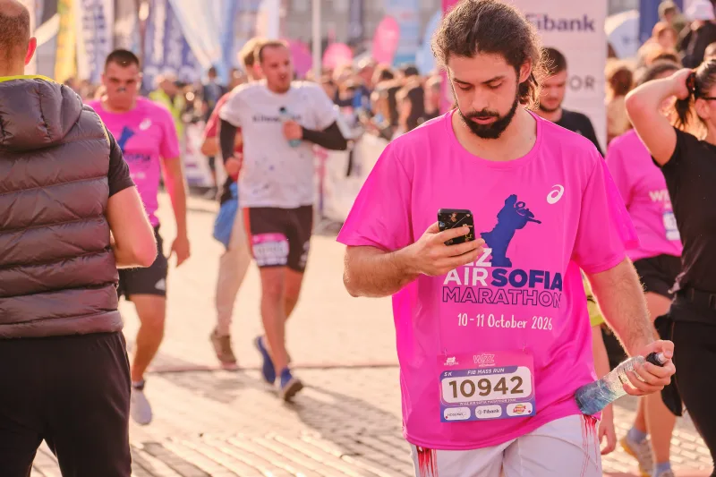 A runner in pink looking at his phone while walking.