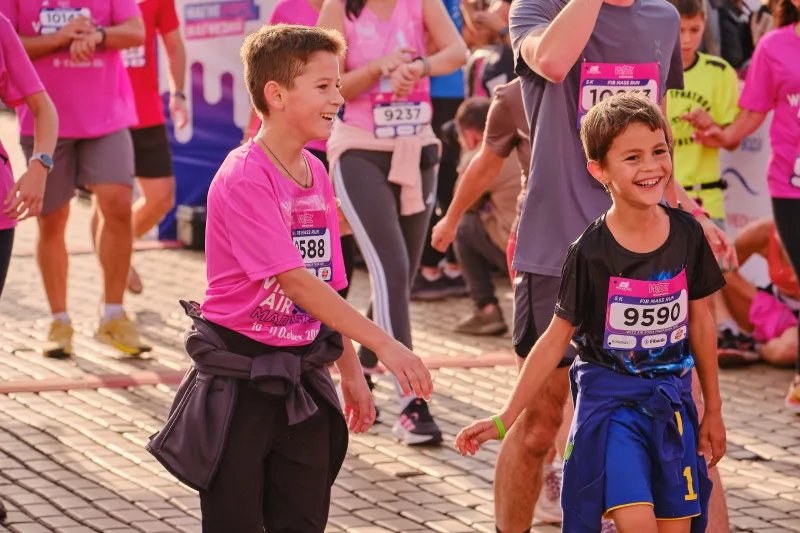 Two smiling young participants in pink and black shirts walking together.