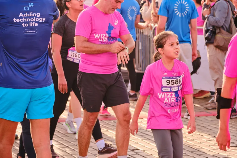 A young participant in pink looking up at a runner beside her.