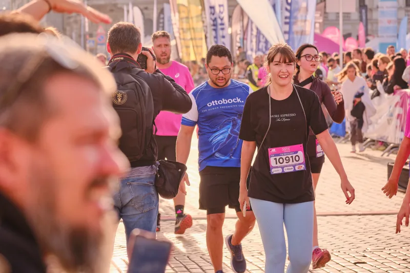 A woman in a black shirt walking among runners beside the barriers.