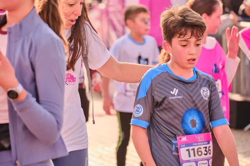 A young runner in a blue-grey sports shirt looking down.