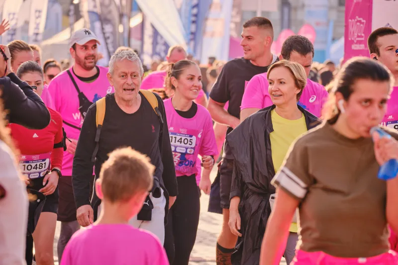 A smiling participant in black and purple among runners in pink.