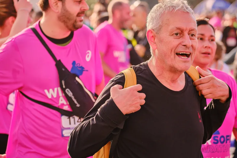 A smiling runner in black holding the straps of a yellow backpack.