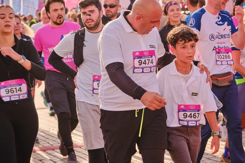 A man in a pale long-sleeved shirt walking beside a young participant.