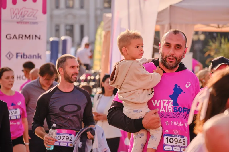 A runner in pink holding a small child as he moves through the crowd.