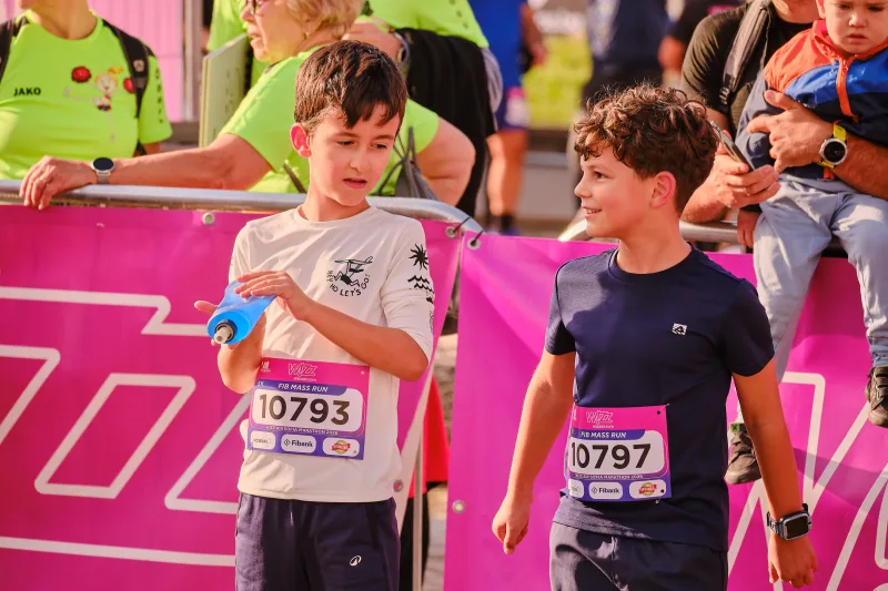 Two young participants in white and navy chatting beside a pink banner.