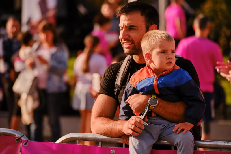 A man in black carrying a small child wearing blue.