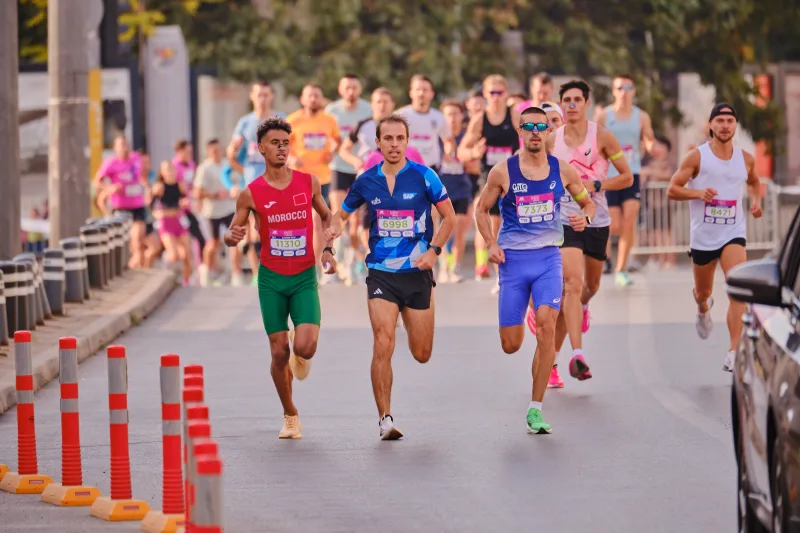 A group of runners approaching along the road beside red-and-white bollards.