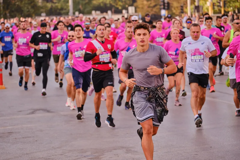 A runner in a grey shirt approaching ahead of a crowd in pink.