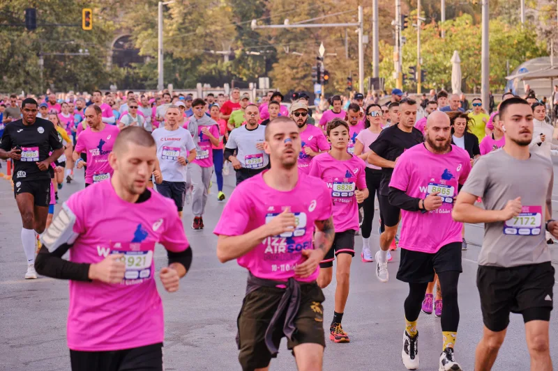 Runners in pink shirts approaching with a large field behind them.