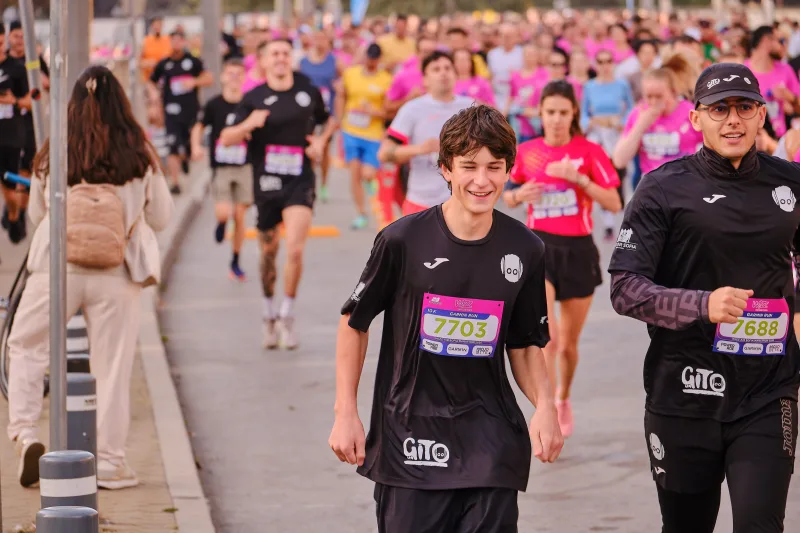 Two smiling participants in black shirts running beside the street barriers.