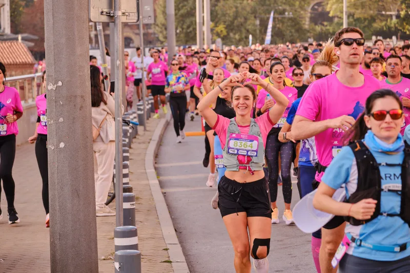 A woman waving as she runs along the road among participants in blue and pink.