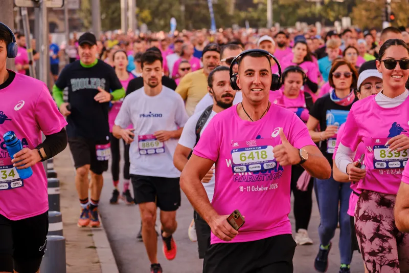 A smiling woman in a pink shirt running through the crowd.