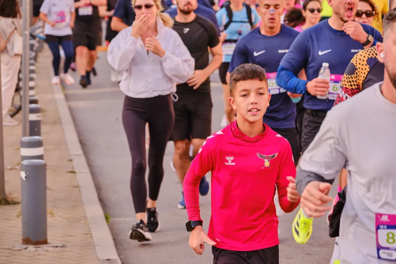 A young runner in a red shirt beside participants in white and blue.