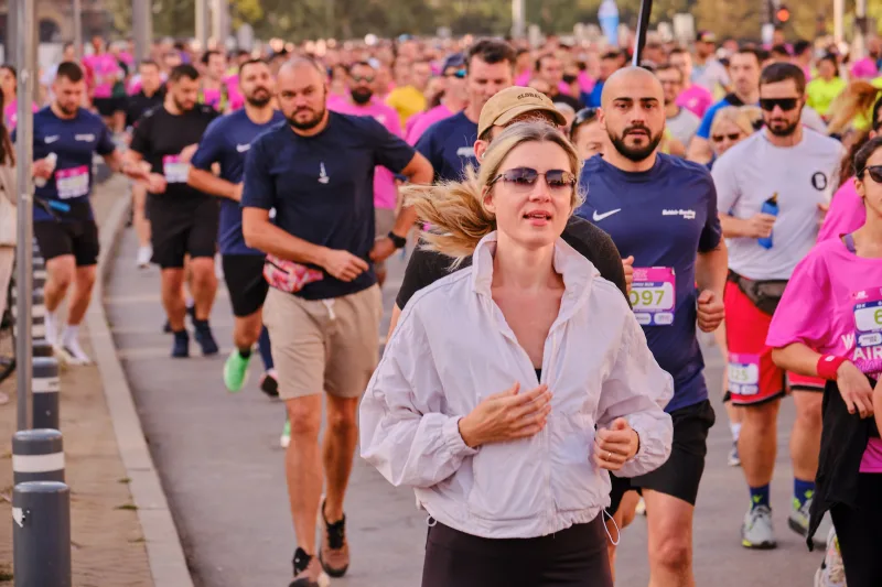 A woman in a white zip-up top and sunglasses running along the road.