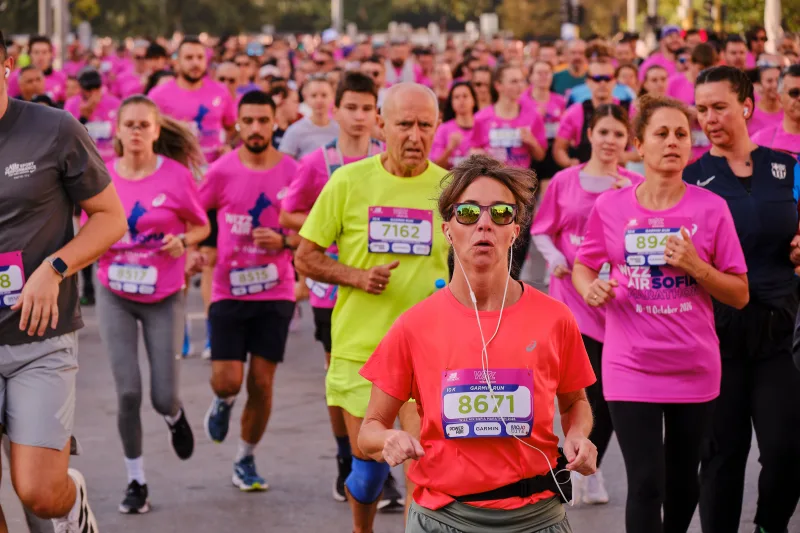 A runner in an orange-red shirt and sunglasses approaching the camera.