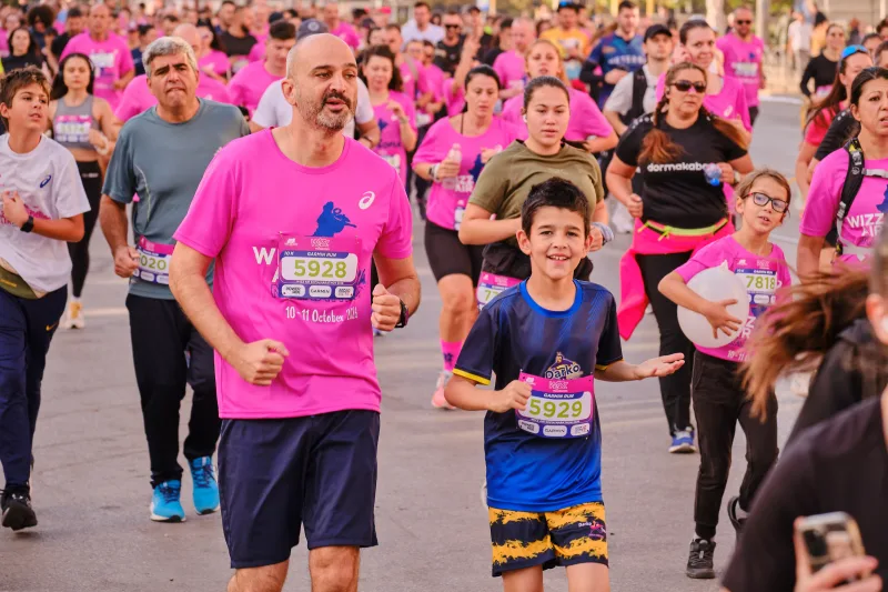 A smiling man in pink running beside a young participant in navy and yellow.