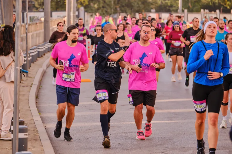 Three runners in pink, black and blue approaching beside the street barriers.