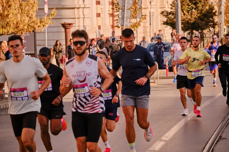 A group of runners in pale and dark tops on the sunlit street.