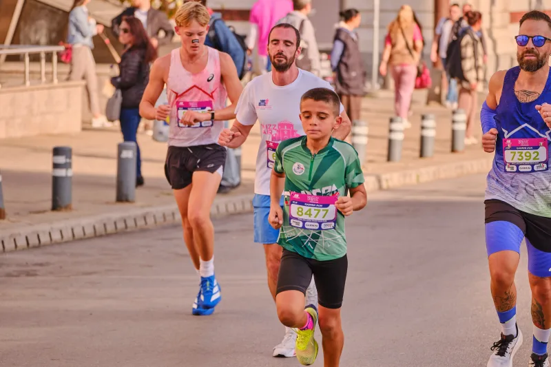 A young runner in green between adults wearing pale and blue vests.