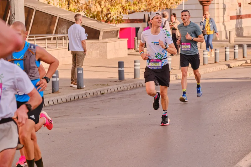 A runner in a grey patterned vest on the sunlit street.