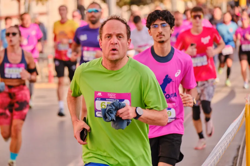 A runner in green approaching with participants in pink behind him.