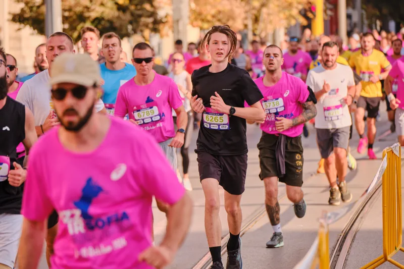Runners in pink and black moving along the sunlit route.